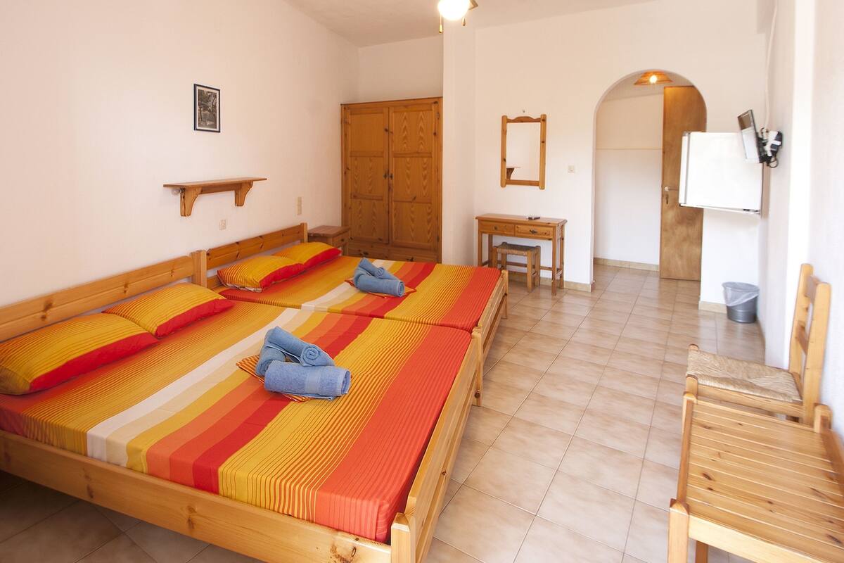 A room with two beds, a desk, a chair, a wardrobe, a mirror, and a ceiling fan.