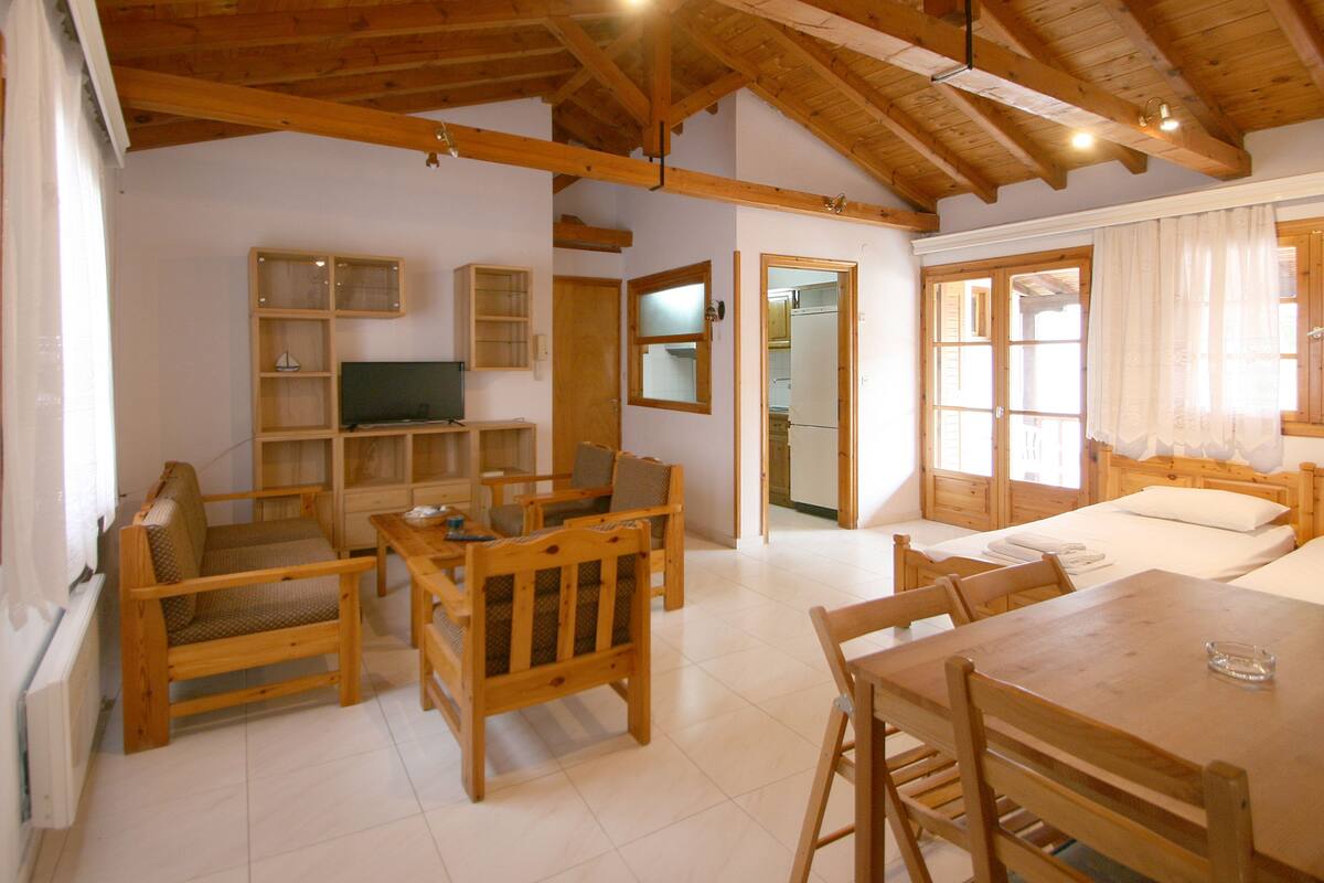 A wooden-furnished room with a dining table, chairs, a TV, and a bed.