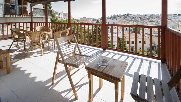 A balcony with wicker furniture and a wooden table, overlooking a cityscape. - Pension Eliza (Skiathos)