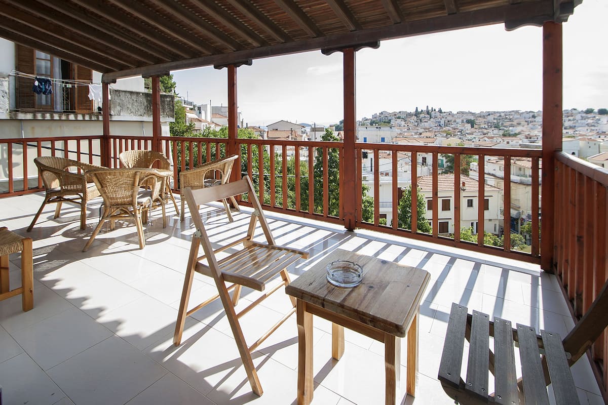 A balcony with wicker furniture and a wooden table, overlooking a cityscape.
