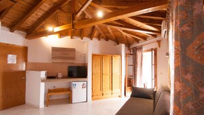 A cozy living room with a sofa, a wooden ceiling, and a small kitchen area with a refrigerator and a microwave. - Pension Eliza (Skiathos)