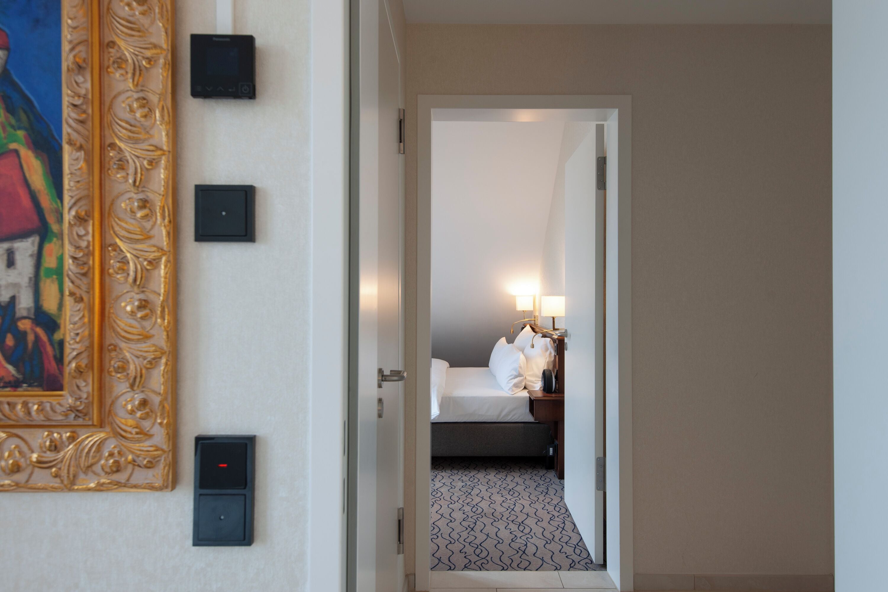 Quarto de hotel com cama, mesa de cabeceira, abajur e um quadro na parede.