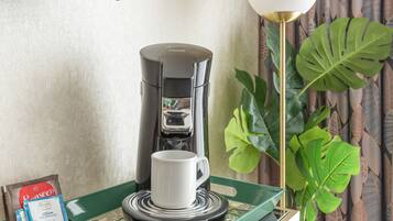 A coffee machine on a table with a cup, a tray of coffee pods, and a plant.