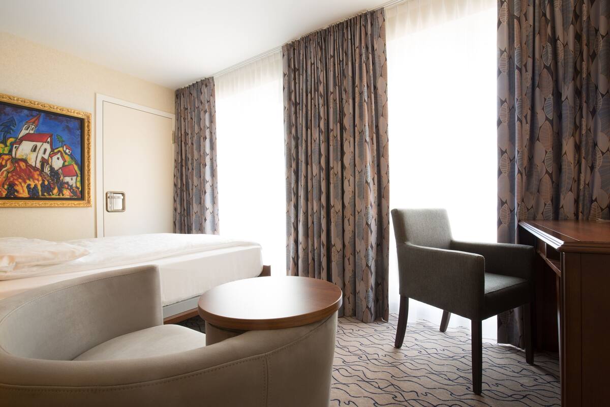 A hotel room with a bed, a desk, a chair, and a painting on the wall.