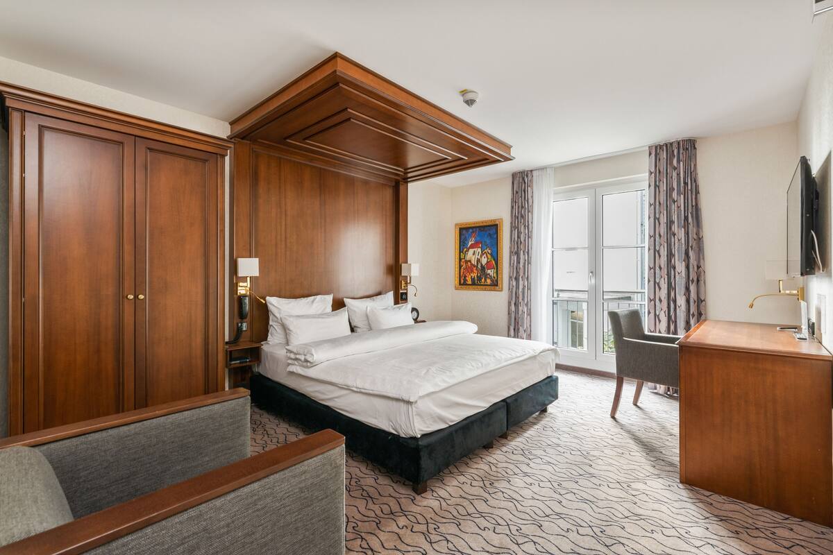 A hotel room with a large bed, a desk, a chair, and a wardrobe.