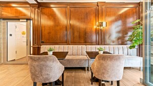 A lobby with a wooden panel wall, a seating area with a sofa and armchairs, and a potted plant. - AdvaStay by KING's (Munich)