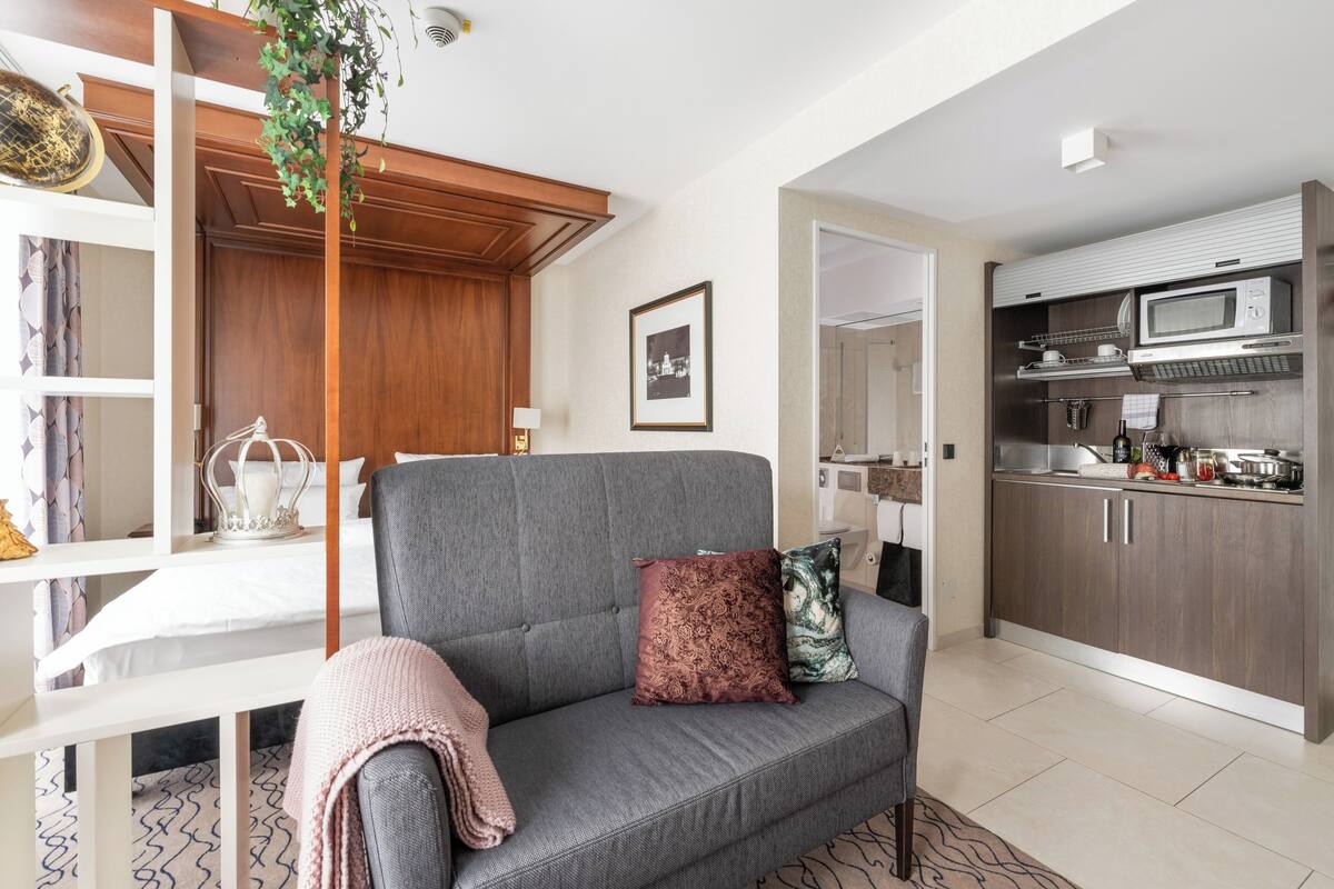 A modern living room with a grey sofa, a small table, and a kitchen area with a microwave and cabinets.