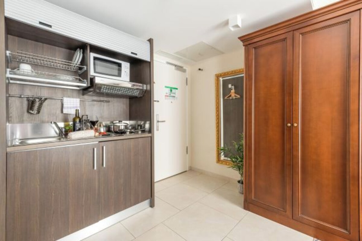 A modern kitchen with wooden cabinets, a microwave, and a sink. There is a wooden door and a potted plant in the corner.