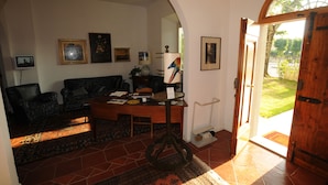 A living room with a sofa, a coffee table, and a desk with a lamp. There is a door leading outside.