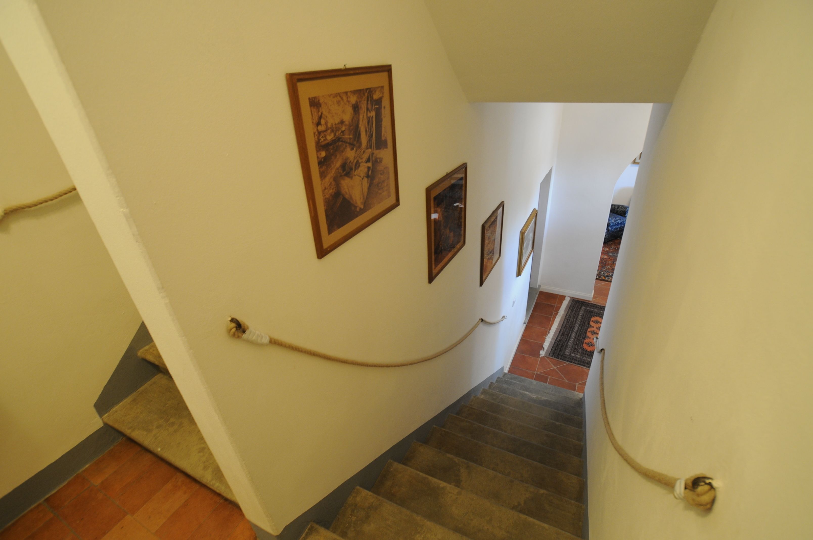 A staircase with a handrail, a doormat at the bottom, and framed pictures on the wall.