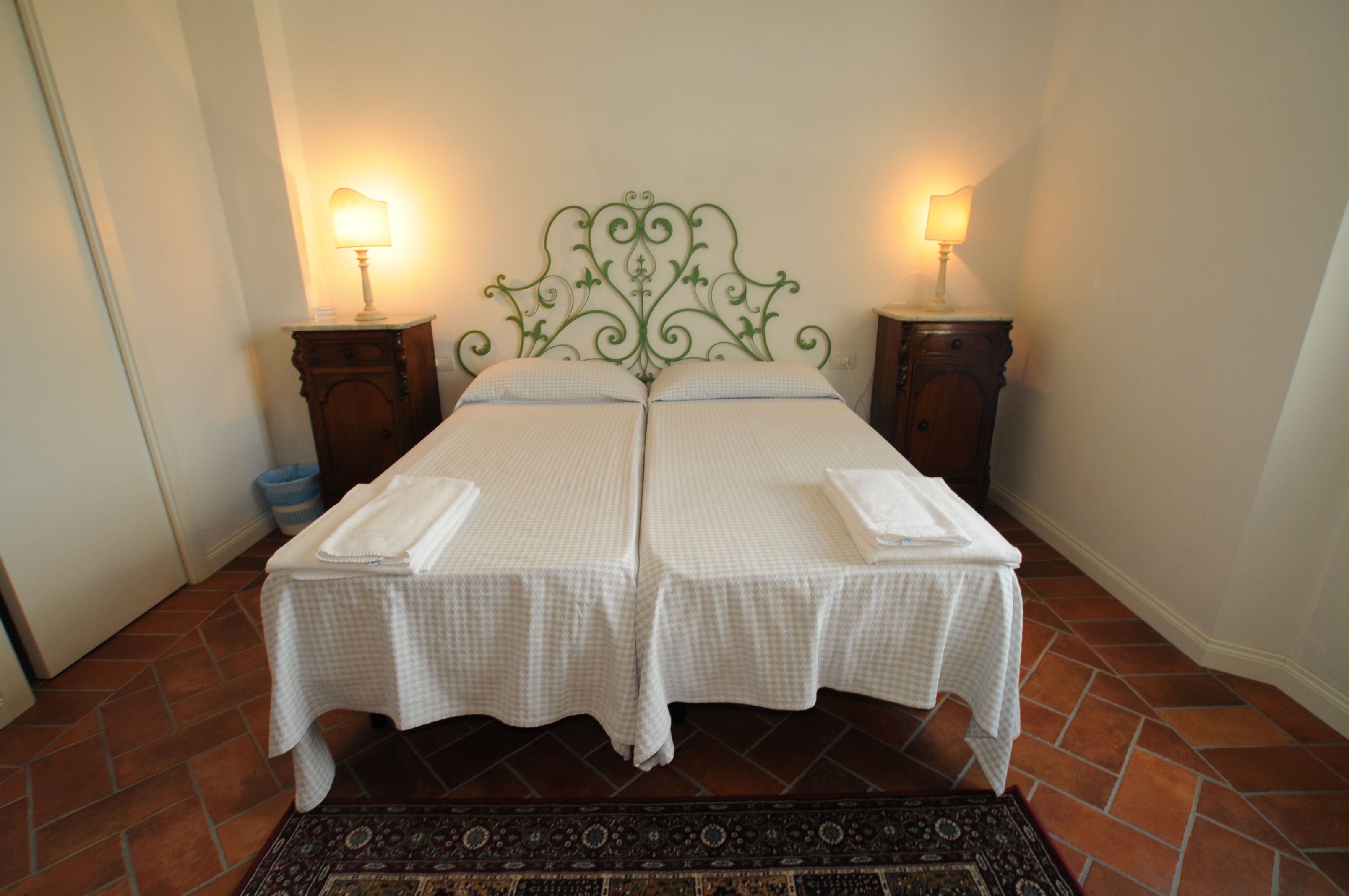 Un letto matrimoniale con testiera in metallo verde, due comodini con lampade e una coperta a quadri.