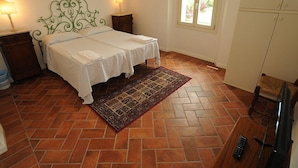 A bedroom with a double bed, two bedside tables with lamps, a patterned rug, a television, and a wardrobe.