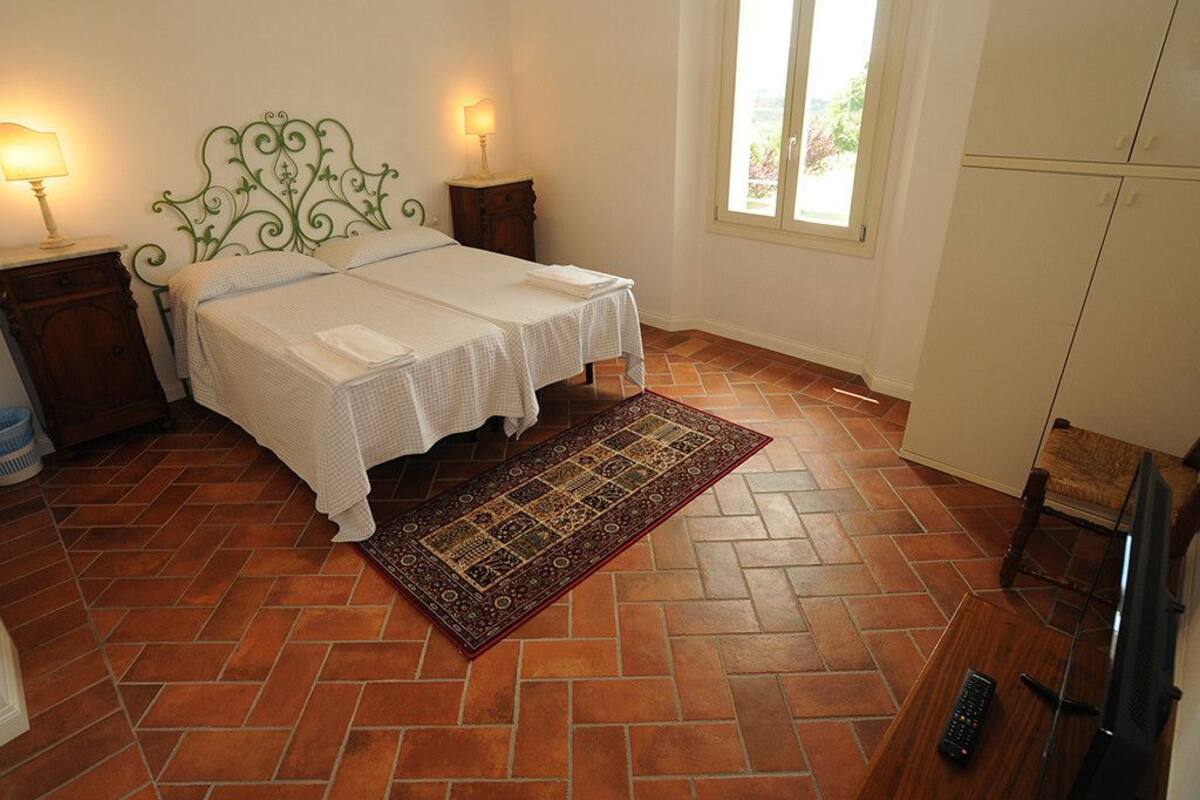 Ein Schlafzimmer mit einem Doppelbett, zwei Nachttischen mit Lampen, einem gemusterten Teppich, einem Fernseher und einem Kleiderschrank.