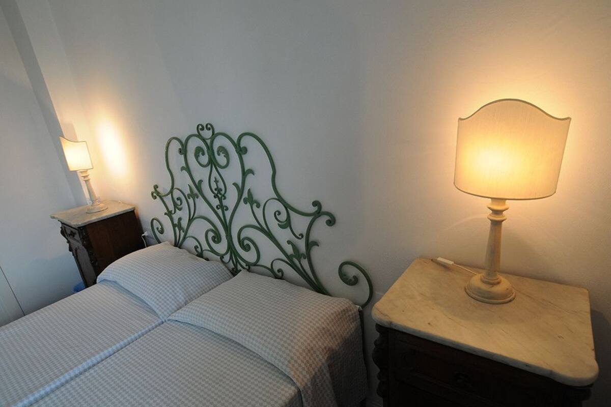 Ein Bett mit Metallkopfteil, zwei Nachttische mit Lampen und eine schlichte Wand.