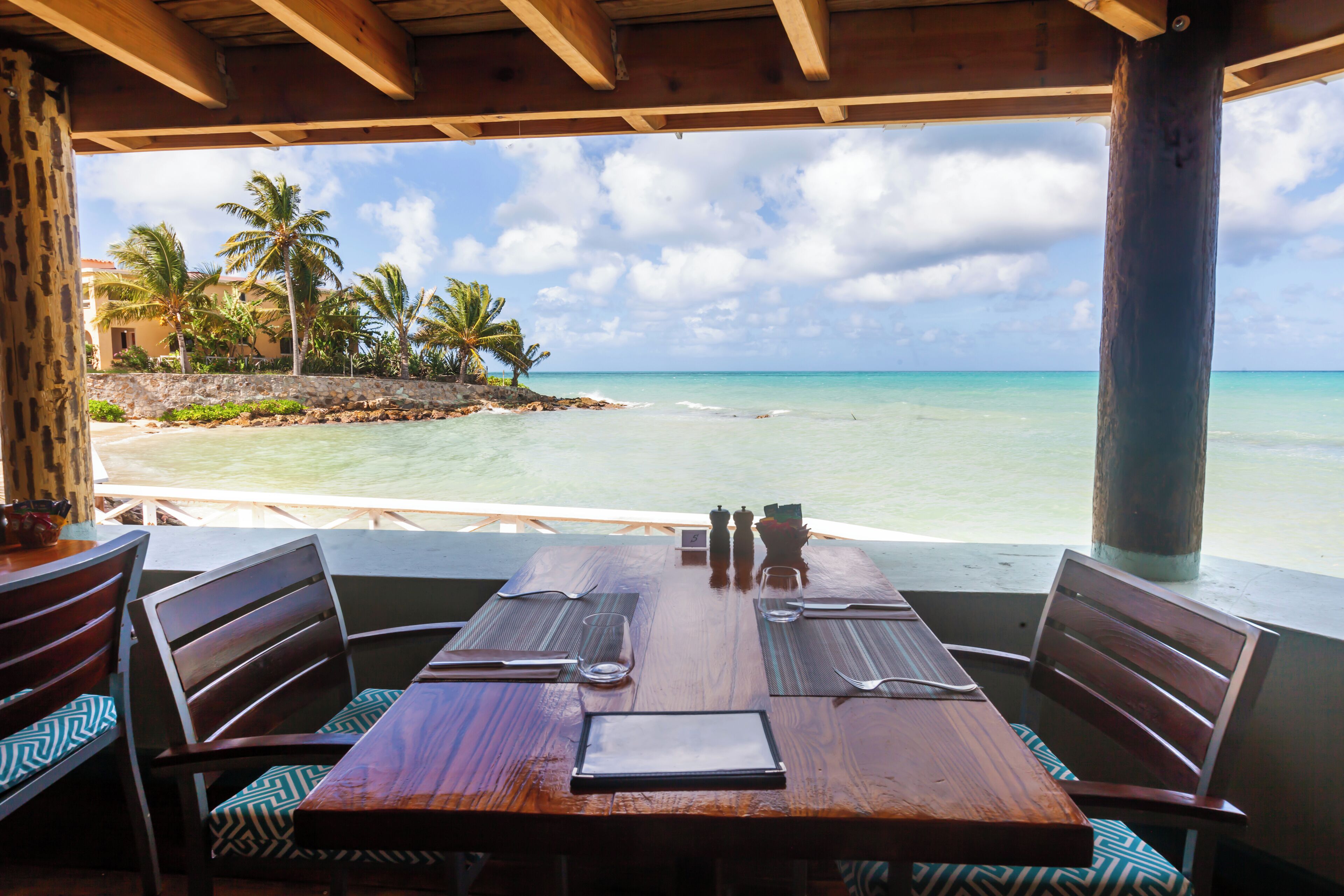 A wooden table with chairs and a view of a beach and palm trees.