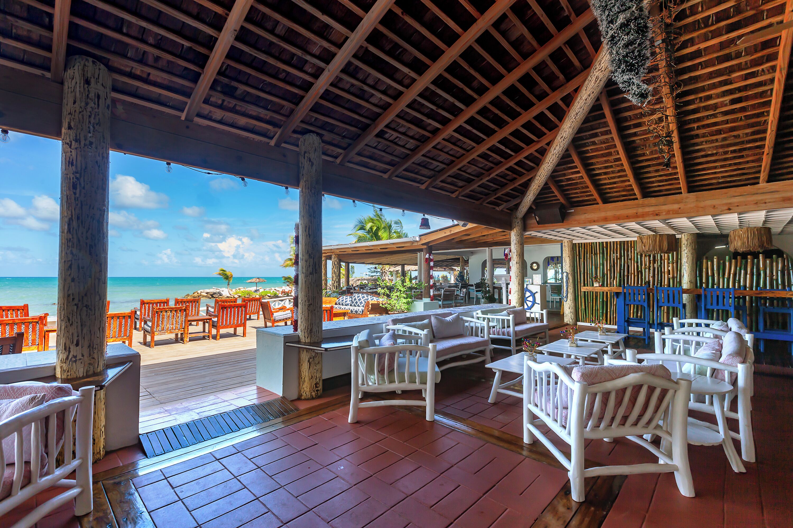 A covered outdoor seating area with wooden tables and chairs, overlooking a beach.