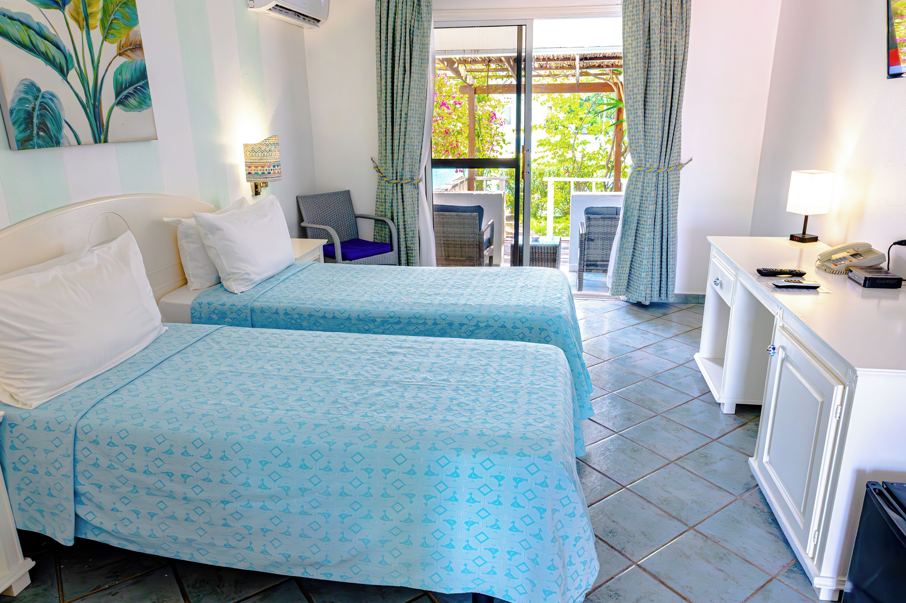 A hotel room with two beds, a desk, a chair, and a balcony with a view.
