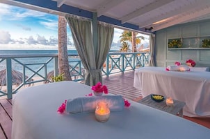 Un spa frente al mar con dos camillas de masaje, una terraza de madera y vistas al océano.