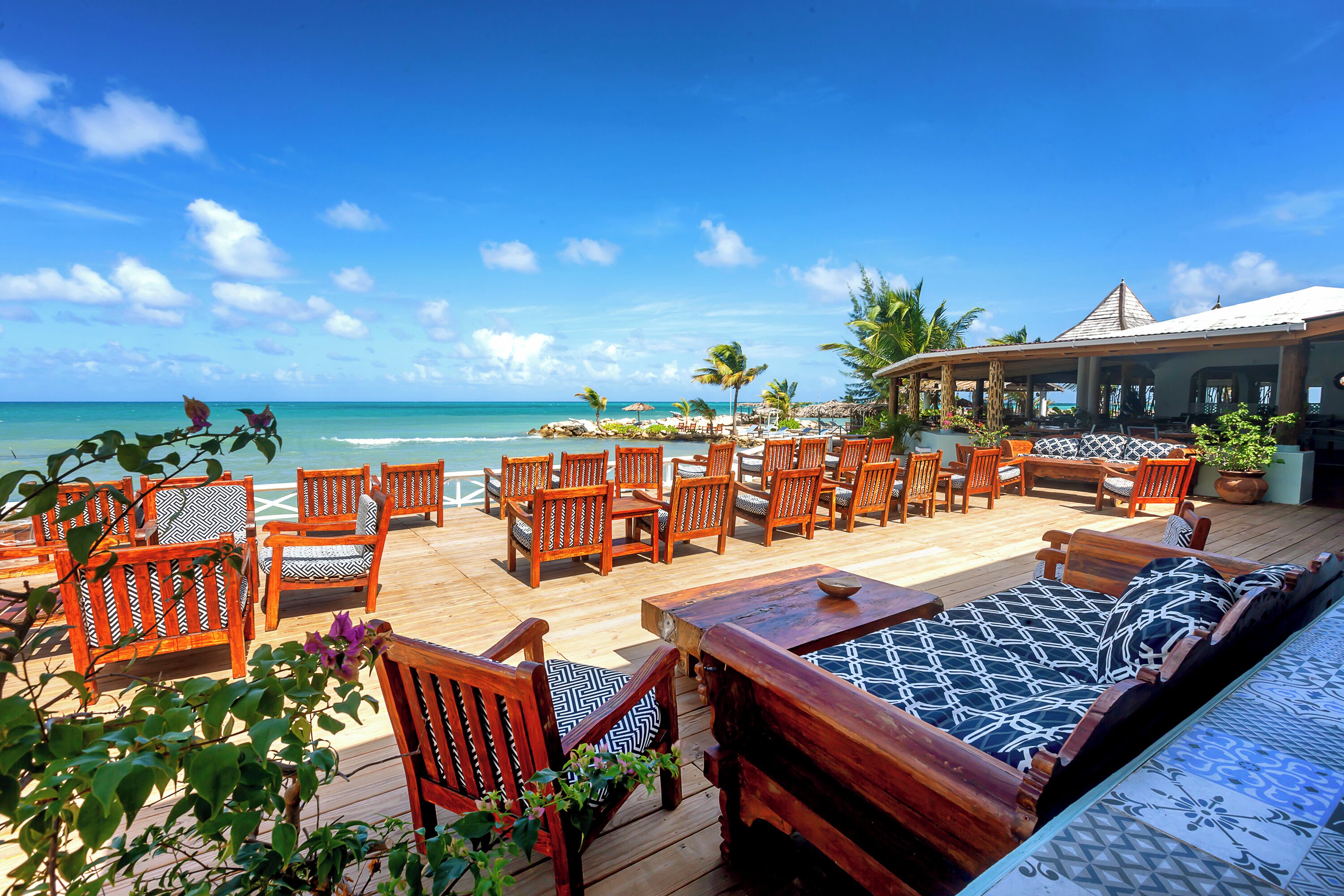 A wooden deck with outdoor seating, overlooking a beach and ocean.