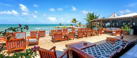 A wooden deck with outdoor seating, overlooking a beach and ocean.