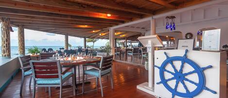 Un espace de restauration en plein air avec des tables et des chaises en bois, une décoration représentant un gouvernail de navire et un panneau affichant le menu.