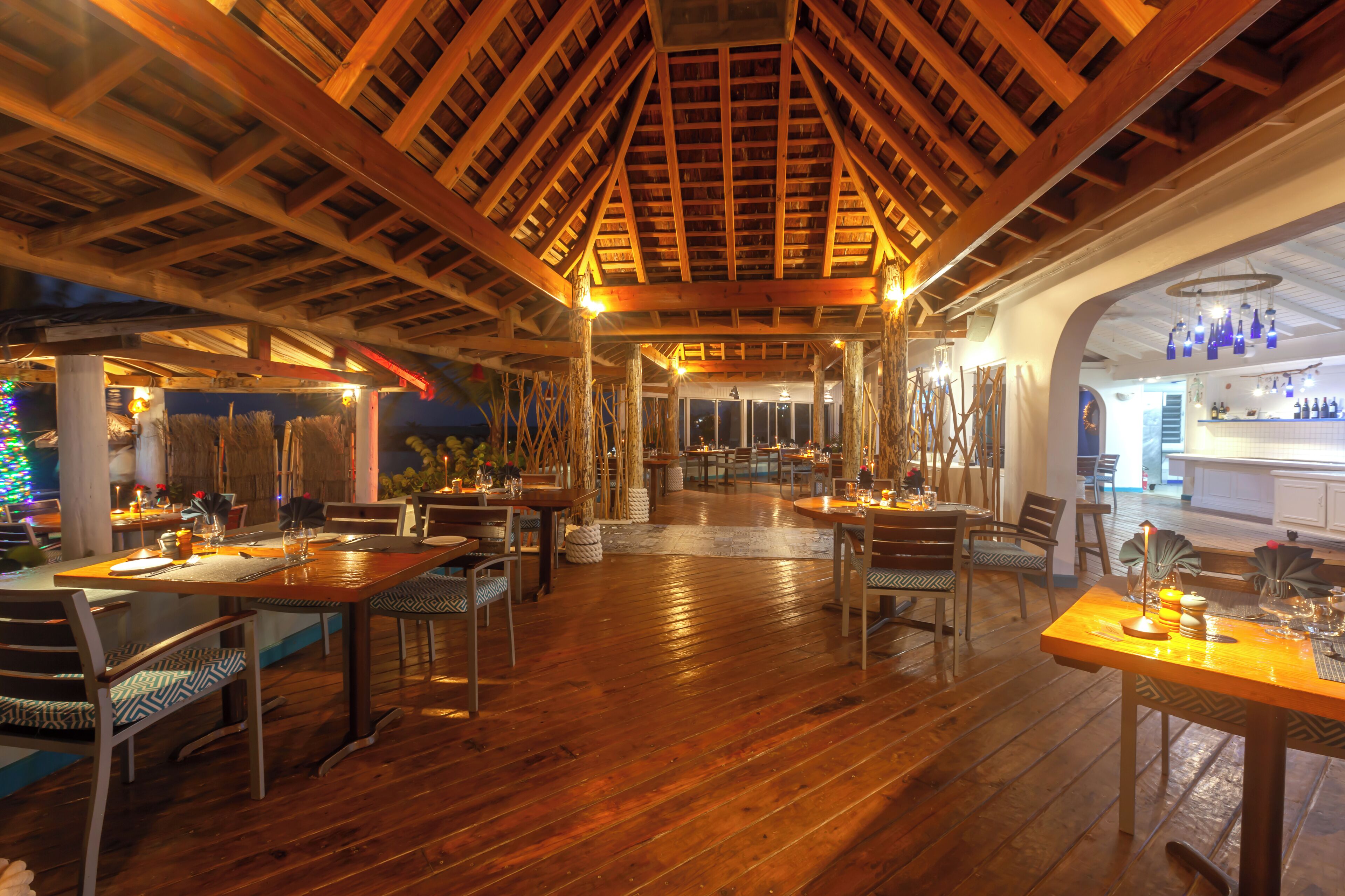 Un restaurant doté de planchers, de tables et de chaises en bois, ainsi que d’un plafond haut avec des poutres apparentes.