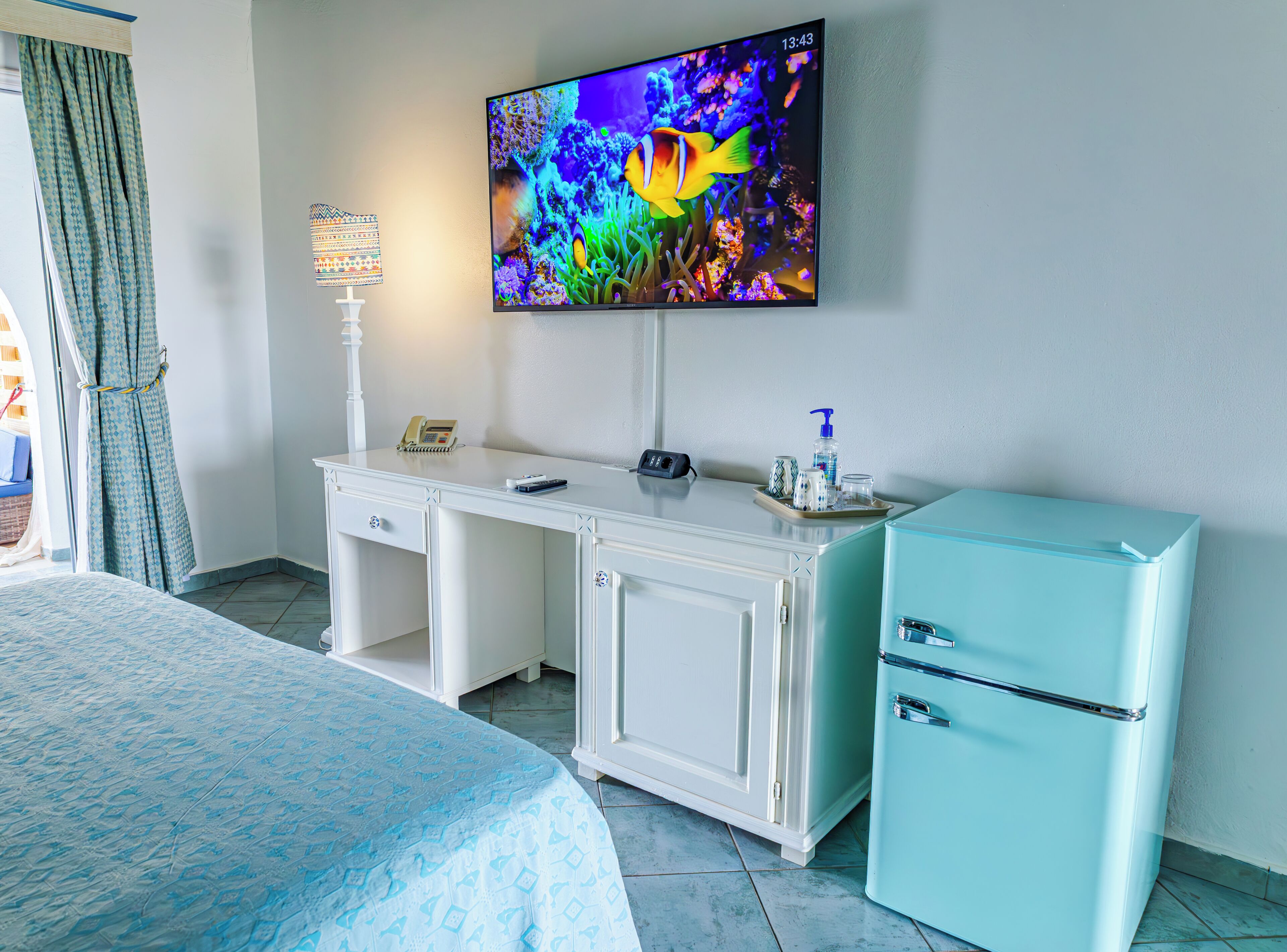 A hotel room with a bed, a desk, a television, and a small refrigerator.