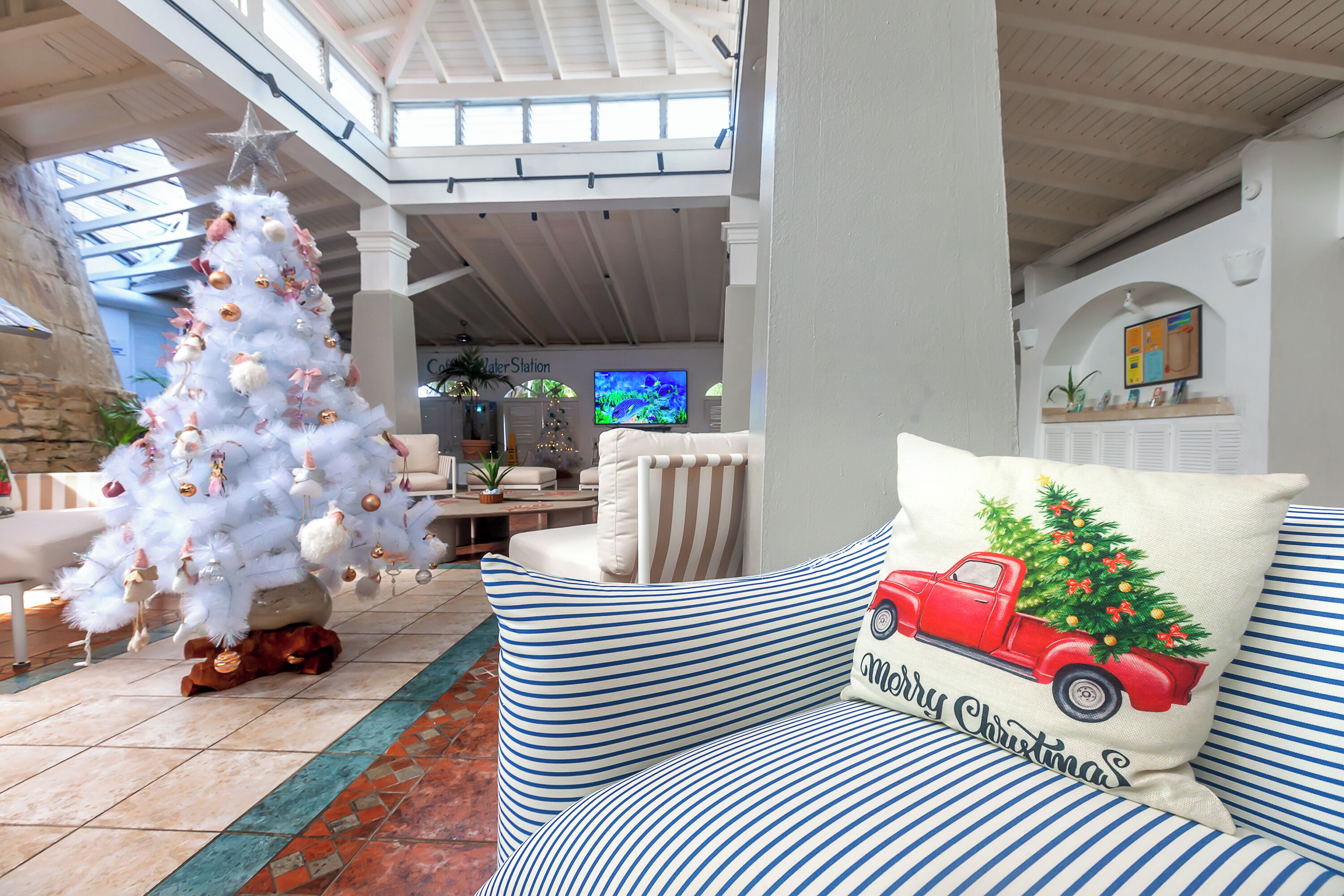 A cozy living room with a white Christmas tree, a red truck-themed pillow, and a television in the background.