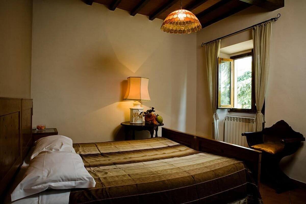 A bedroom with two beds, a lamp, a chair, and a window with curtains.