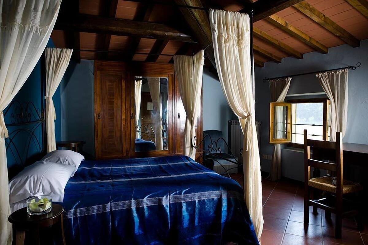 A bedroom with a bed, a wooden wardrobe, a chair, and a window with curtains.