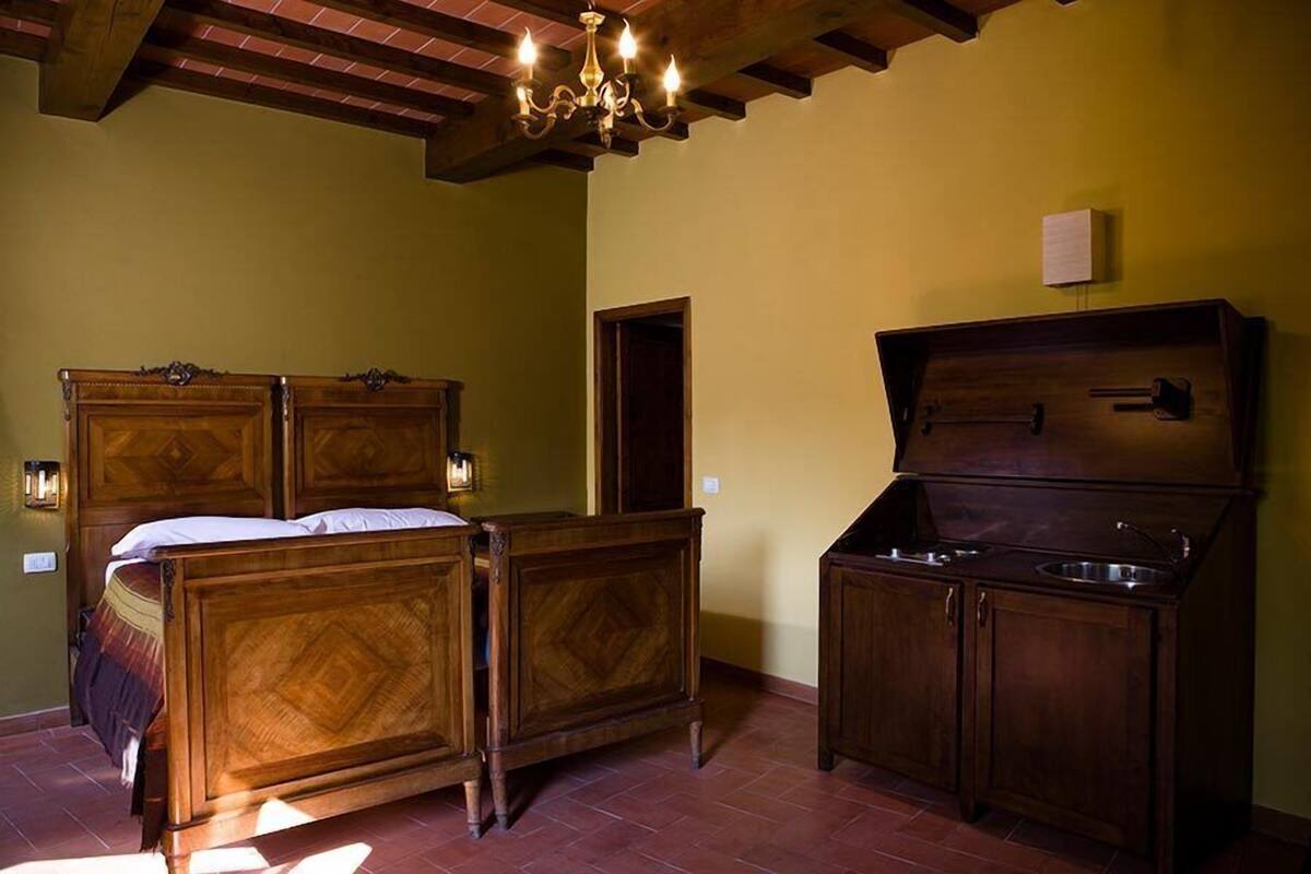 A bedroom with a wooden bed, a chest of drawers, and a small kitchen area with a sink.
