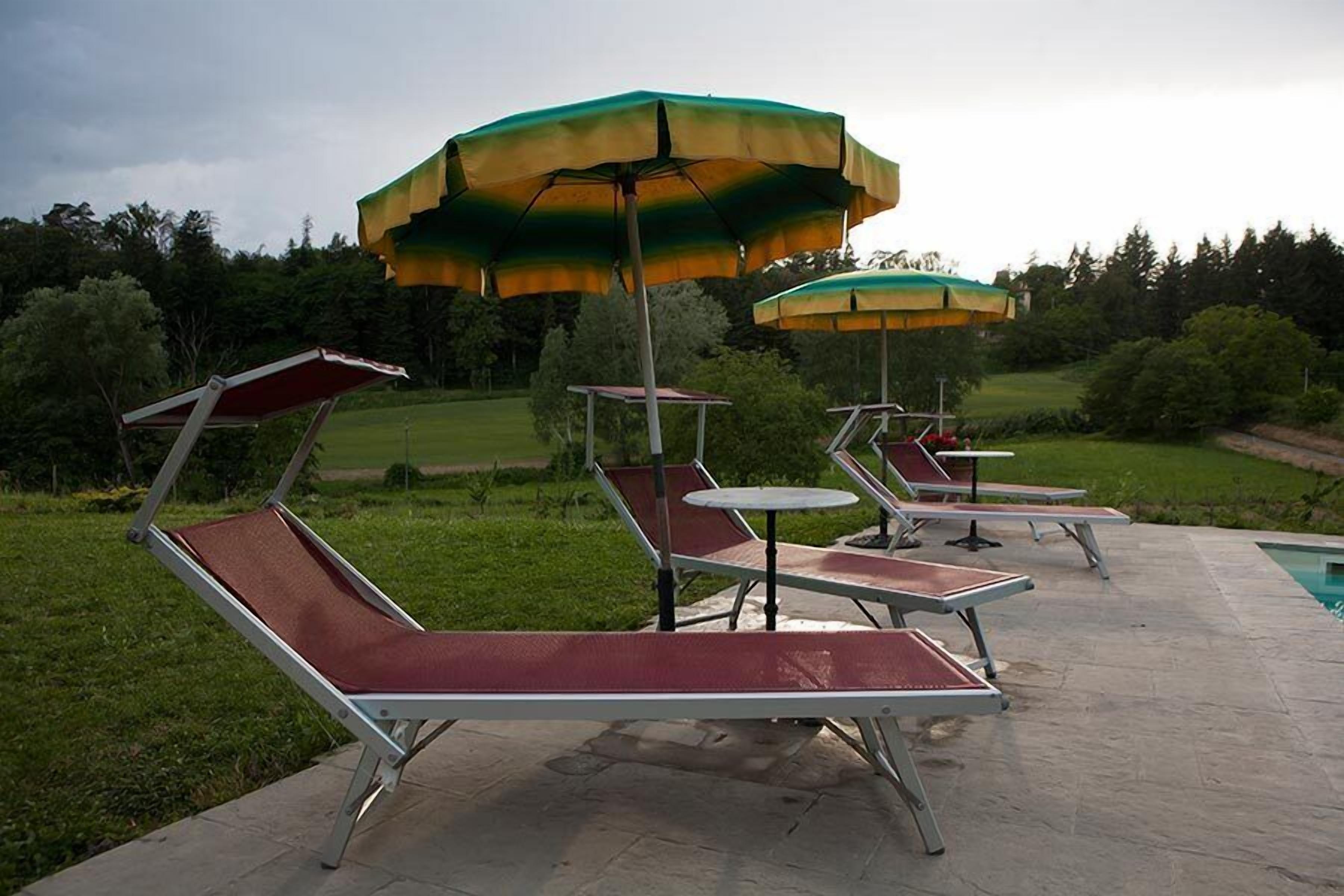 Outdoor lounge chairs with umbrellas, a pool, and a landscaped garden.
