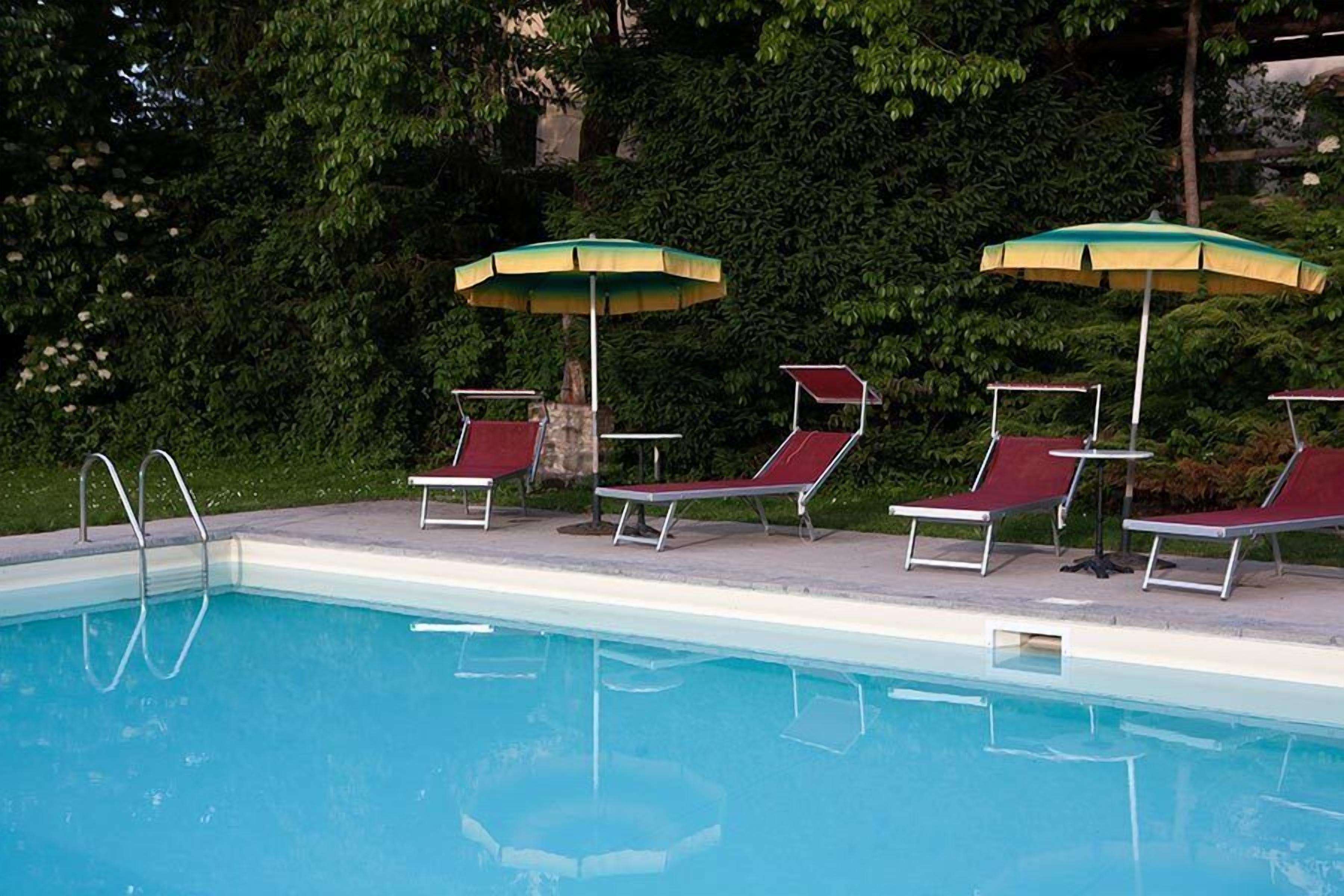 Una piscina con cuatro sillas de descanso y dos sombrillas.