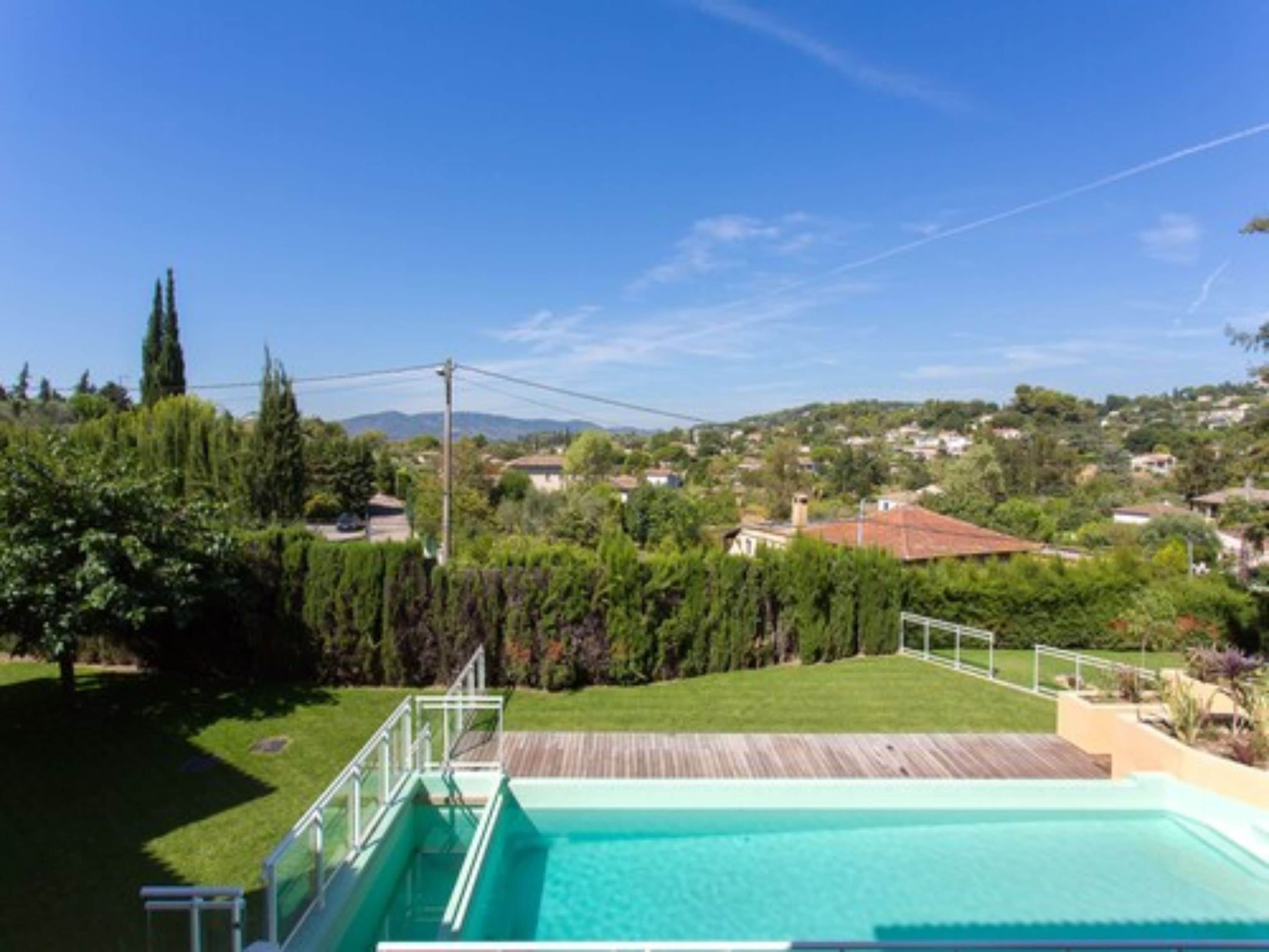 Una piscina con cubierta de madera, rodeada de vegetación y casas al fondo.