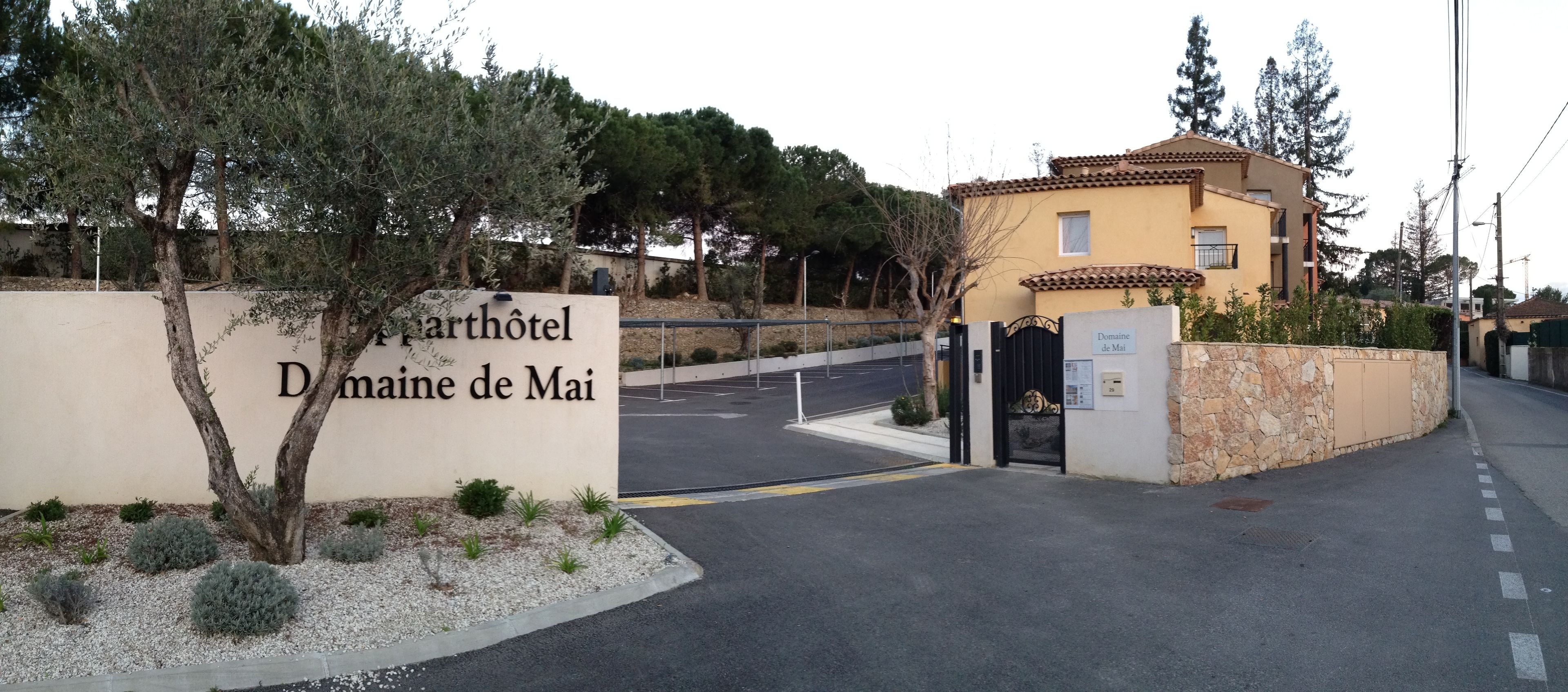A sign for 'Domaine de Mai' with a gated entrance and a building with a tiled roof.