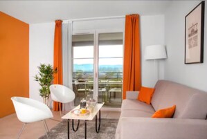 Una sala de estar moderna con un sofá, un sillón blanco, una mesa con alimentos para el desayuno y vistas a través de amplias ventanas.