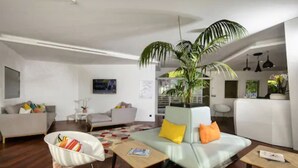 A modern living room with a sofa, armchair, and coffee table. There is a large potted plant in the center. - Adonis Mougins (Mougins)
