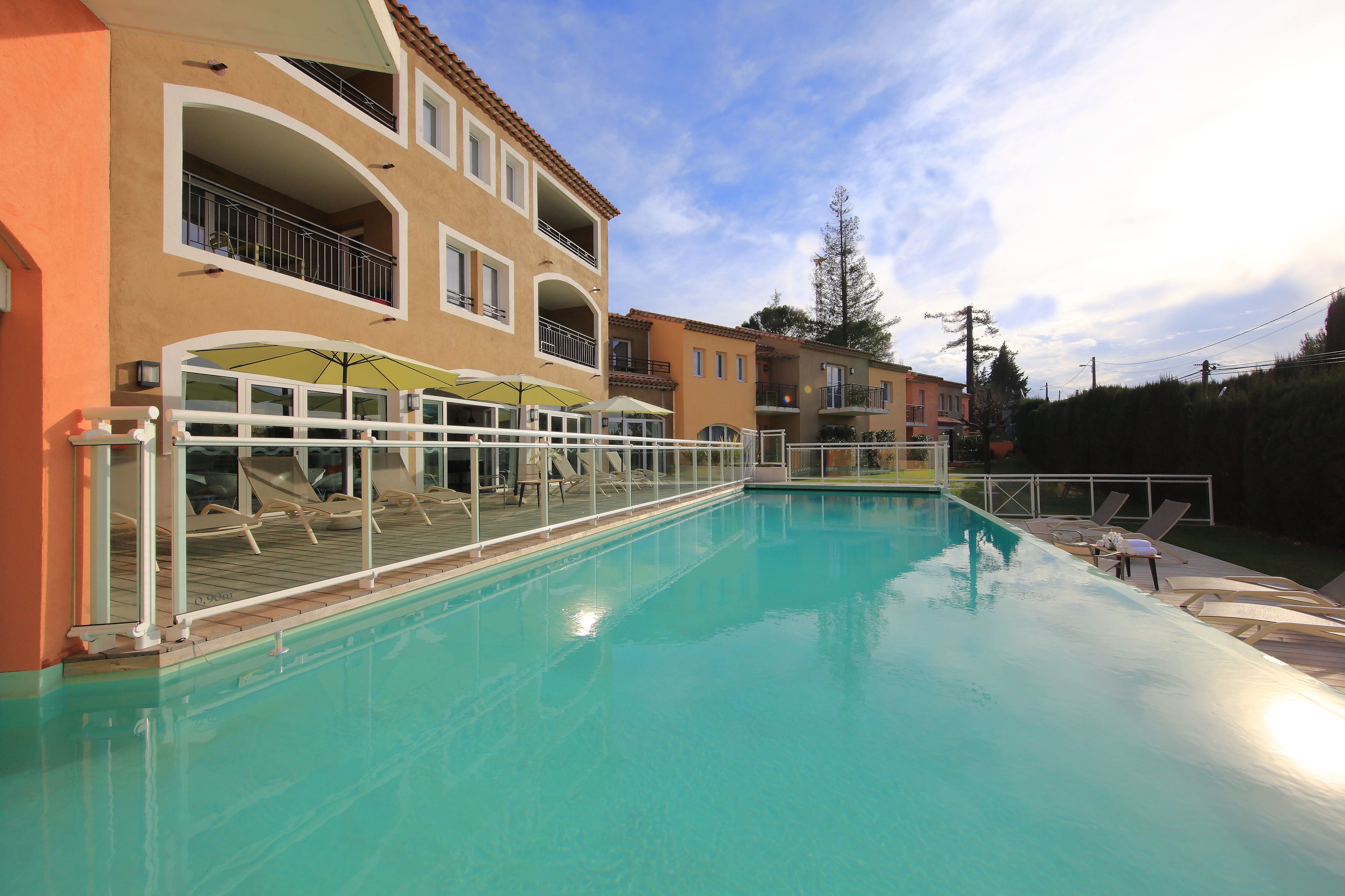 Piscina com espreguiçadeiras e guarda-sóis, rodeada por edifícios altos com varandas.