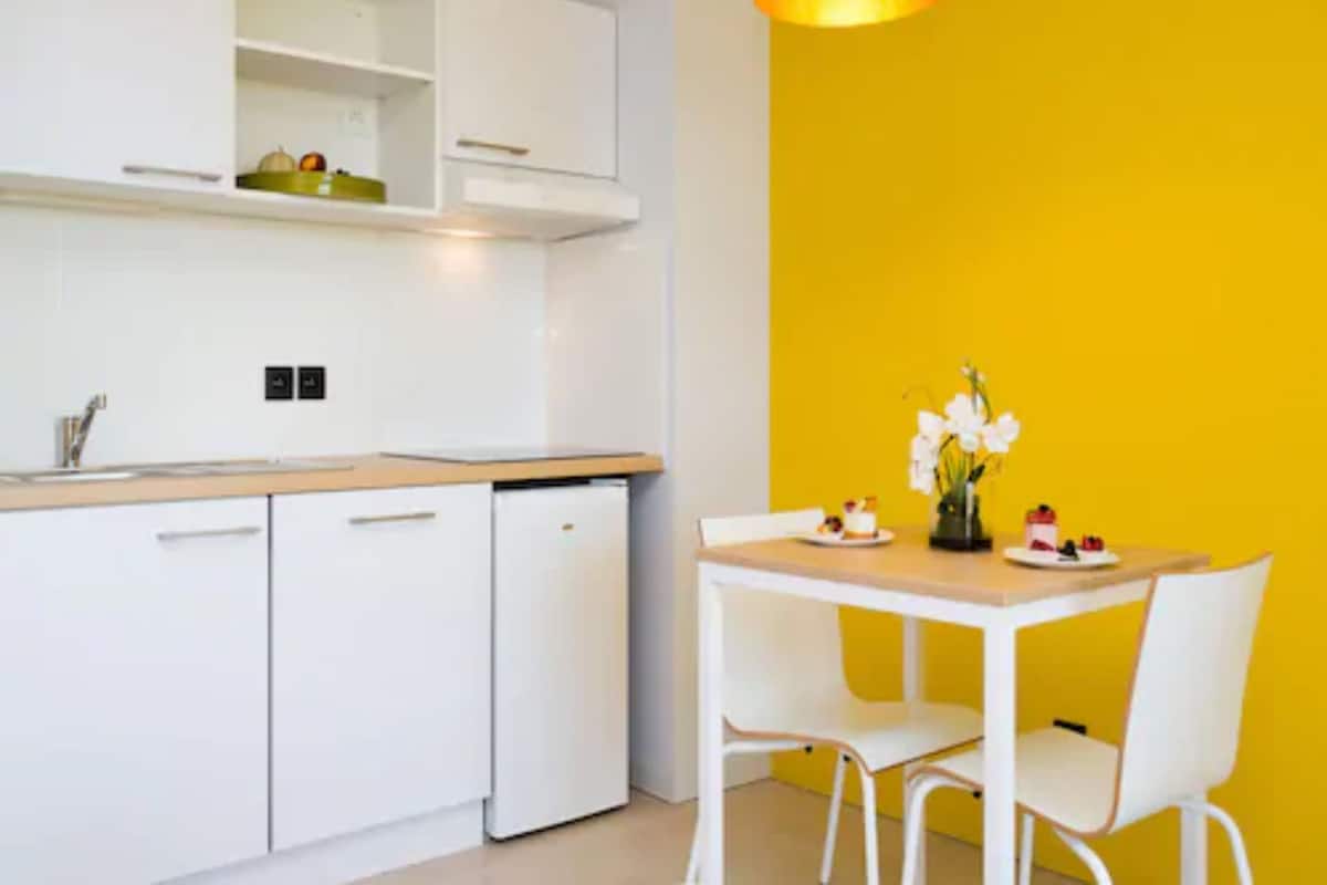 Una cocina moderna con armarios blancos, encimera de madera y una pared de acento amarilla.