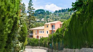 A residential street with a house featuring a balcony, surrounded by lush greenery and a stone wall. - Adonis Mougins (Mougins)