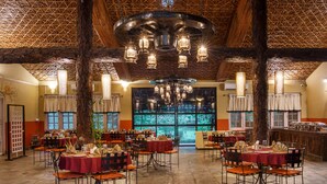 A spacious dining area with multiple tables and chairs, a large chandelier, and a view through large windows. - GREEN MANSIONS JUNGLE RESORT (Sauraha)