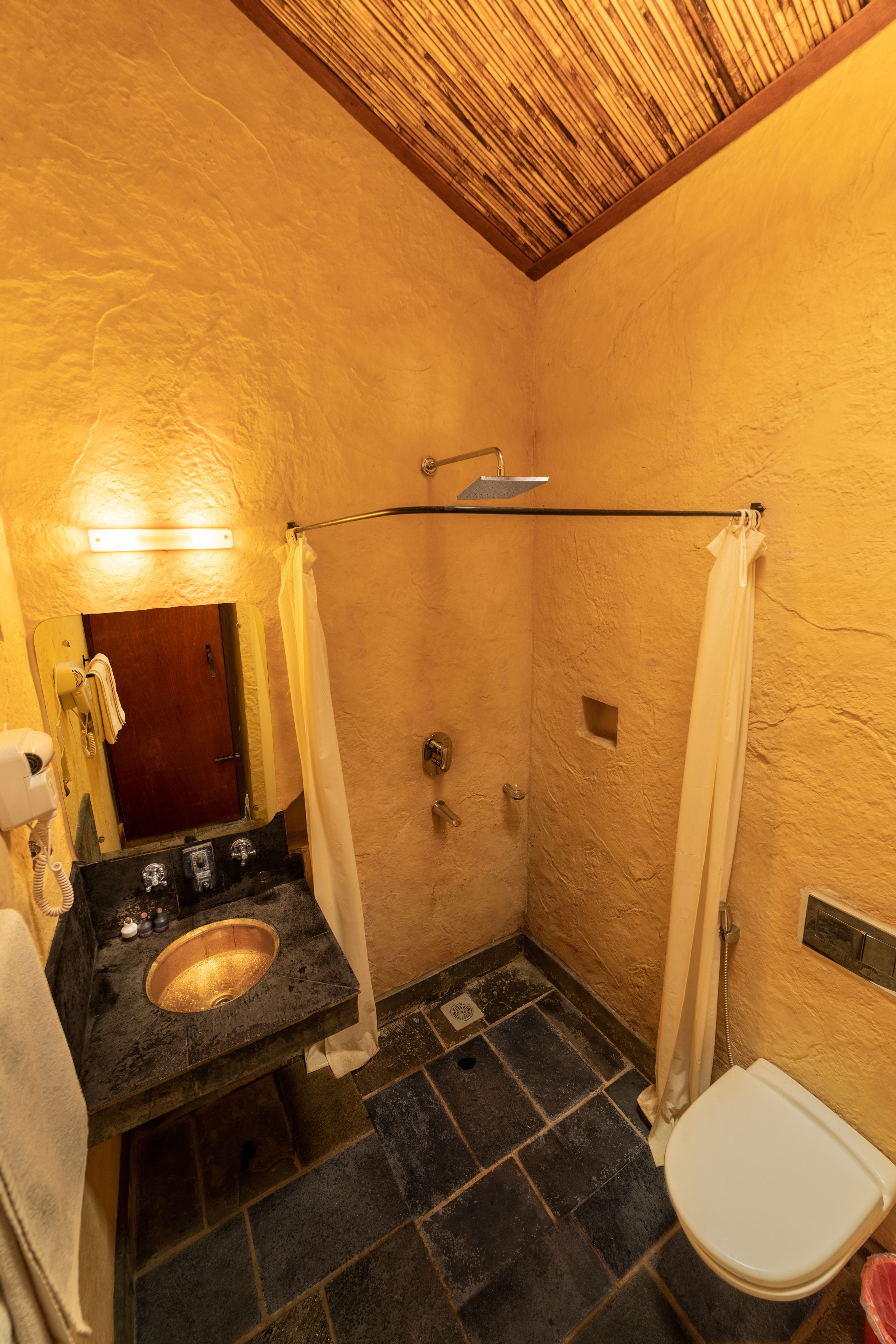 A bathroom with a stone sink, a toilet, and a shower with a wooden ceiling.