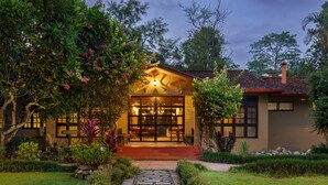 A restaurant with a stone pathway leading to the entrance, surrounded by lush greenery and flowering plants. - GREEN MANSIONS JUNGLE RESORT (Sauraha)