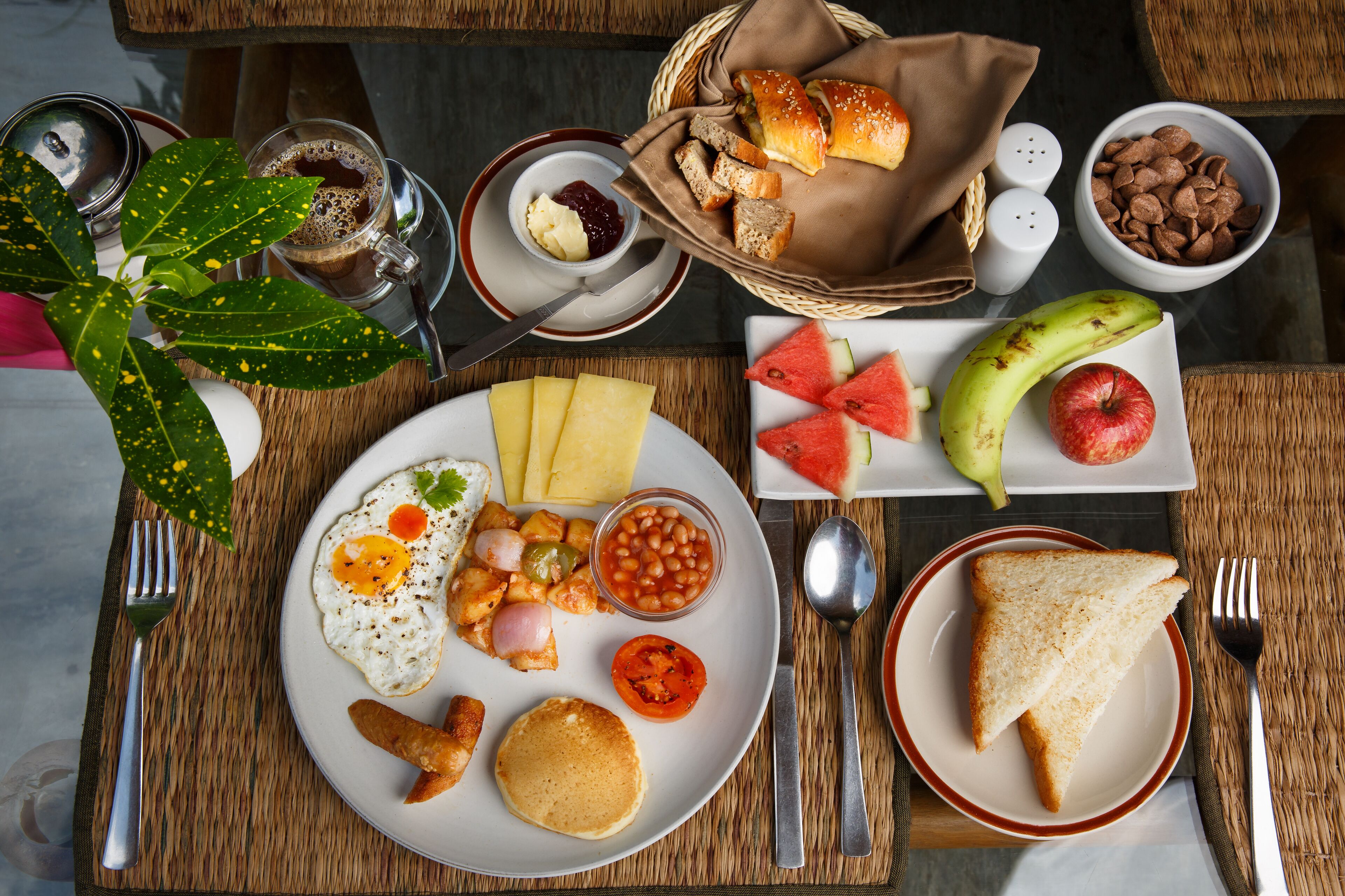 A breakfast table with various food items, including toast, eggs, beans, and fruits.