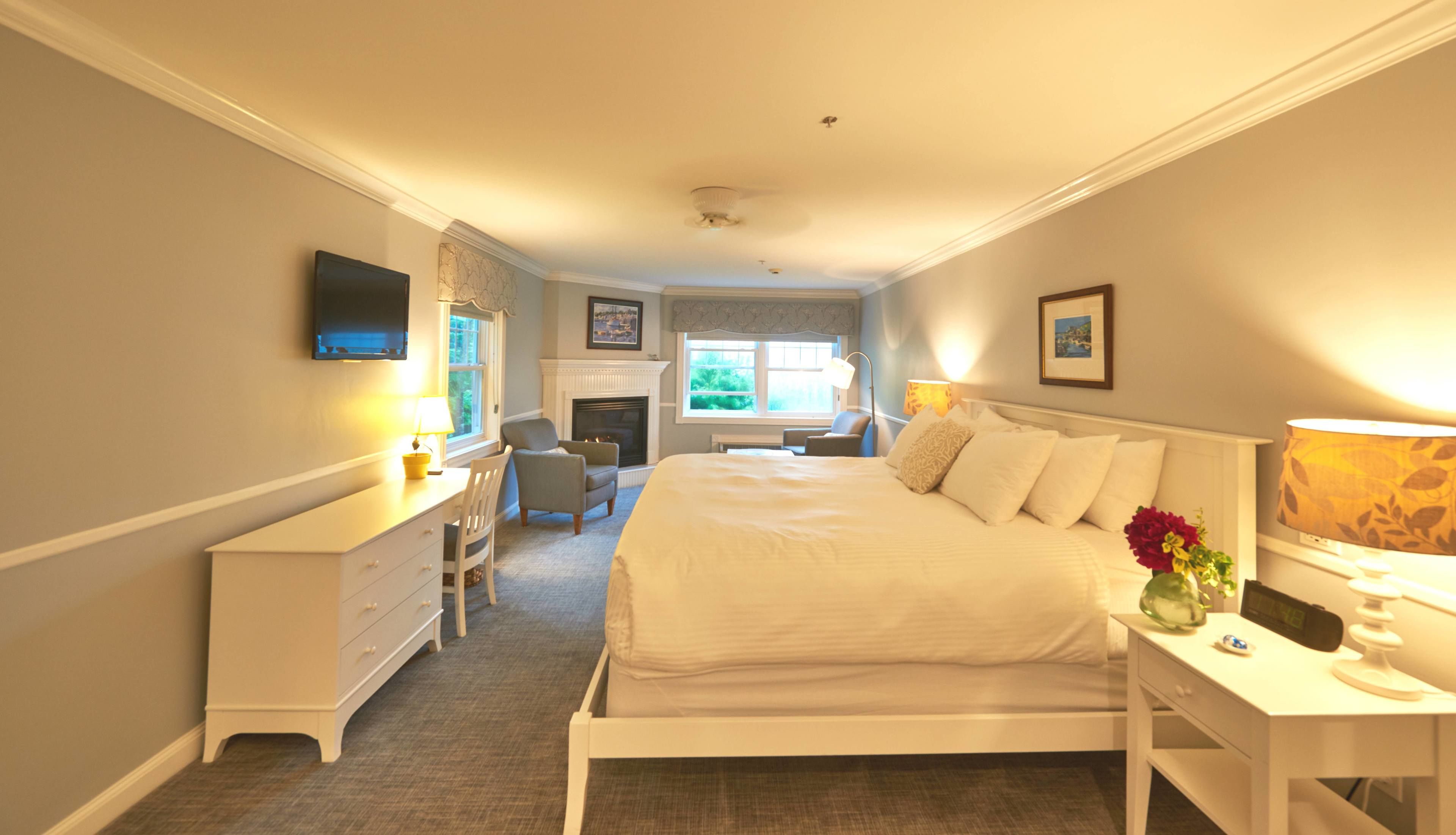 A bedroom with a bed, desk, chair, and a fireplace.