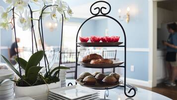 Un présentoir à trois niveaux, orné de pâtisseries et surmonté d’une plante en pot, est posé sur une table.