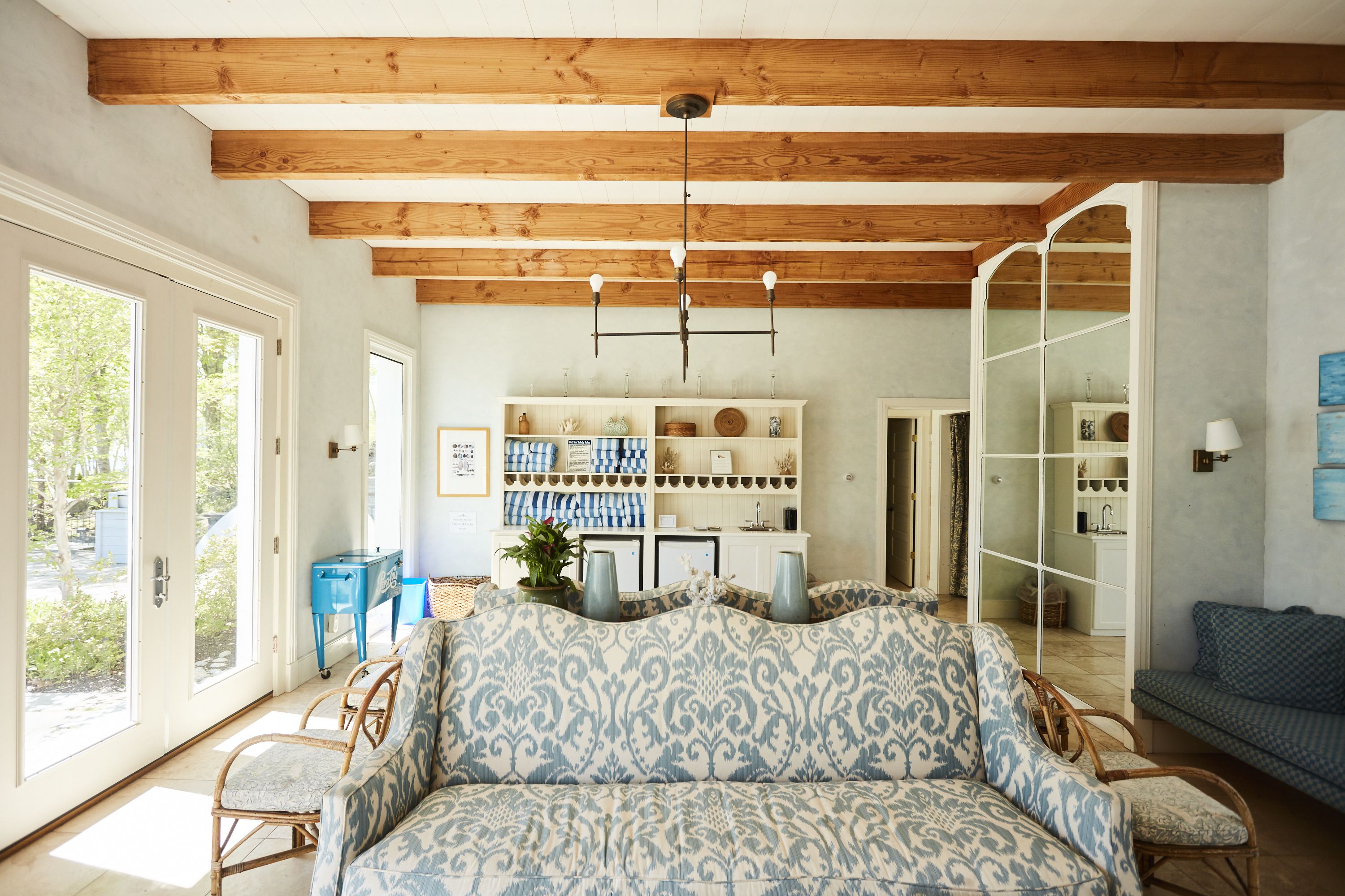A living room with a patterned sofa, wooden beams, a chandelier, and a view through a glass door.