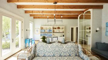 A living room with a patterned sofa, wooden beams, a chandelier, and a view through a glass door.