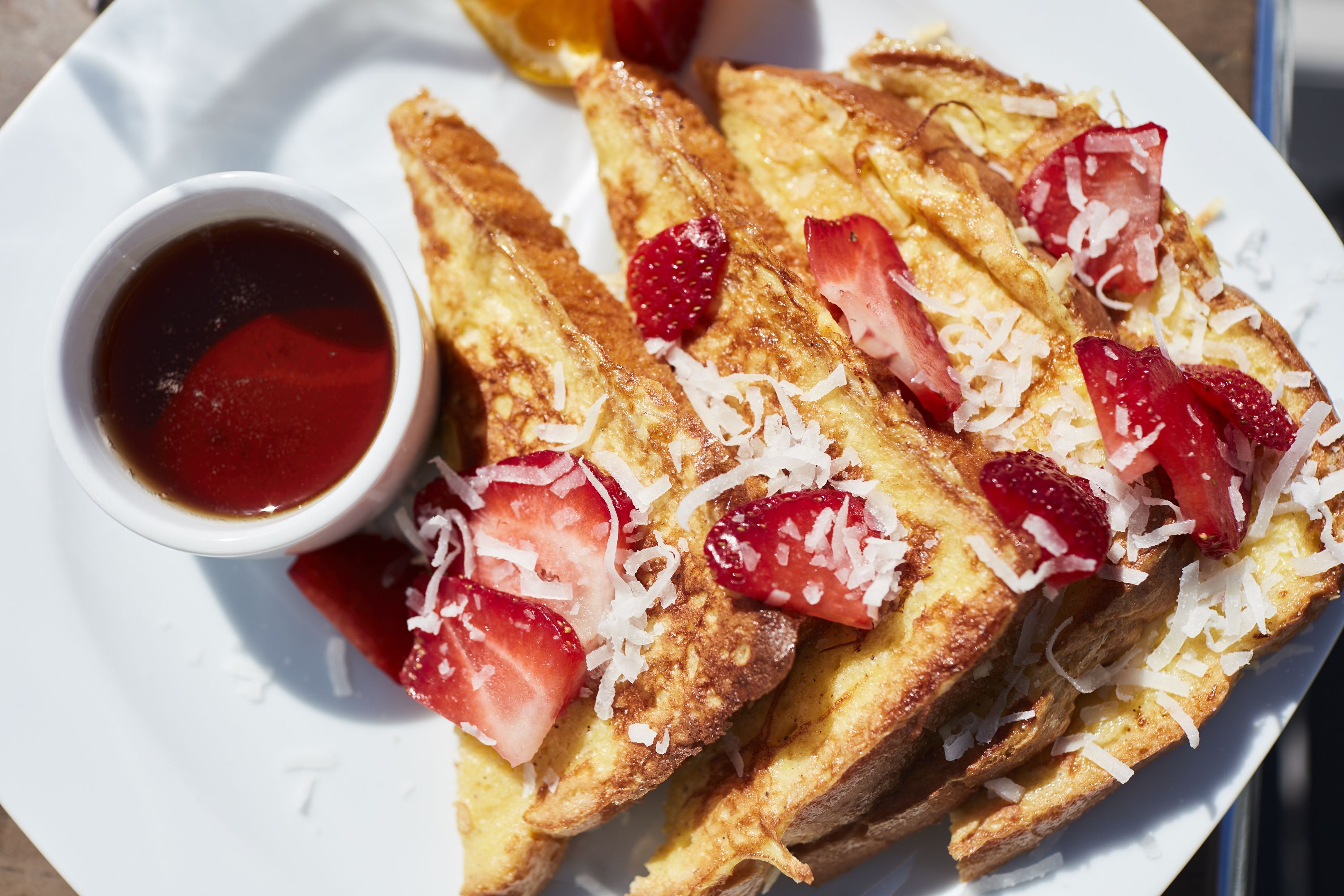 A plate of French toast with strawberries and a small bowl of syrup.