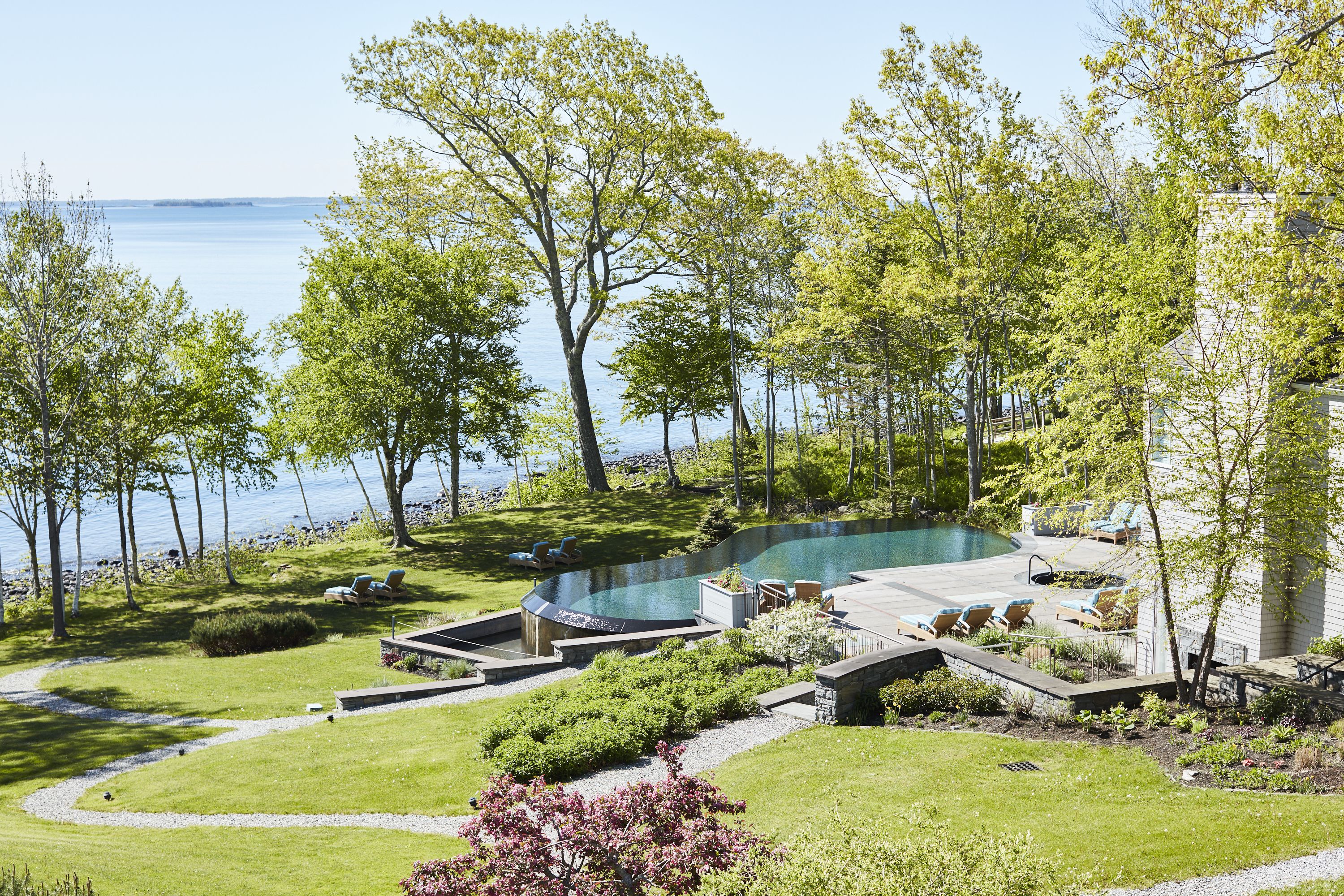A landscaped backyard with a swimming pool, lounge chairs, and a view of the water.